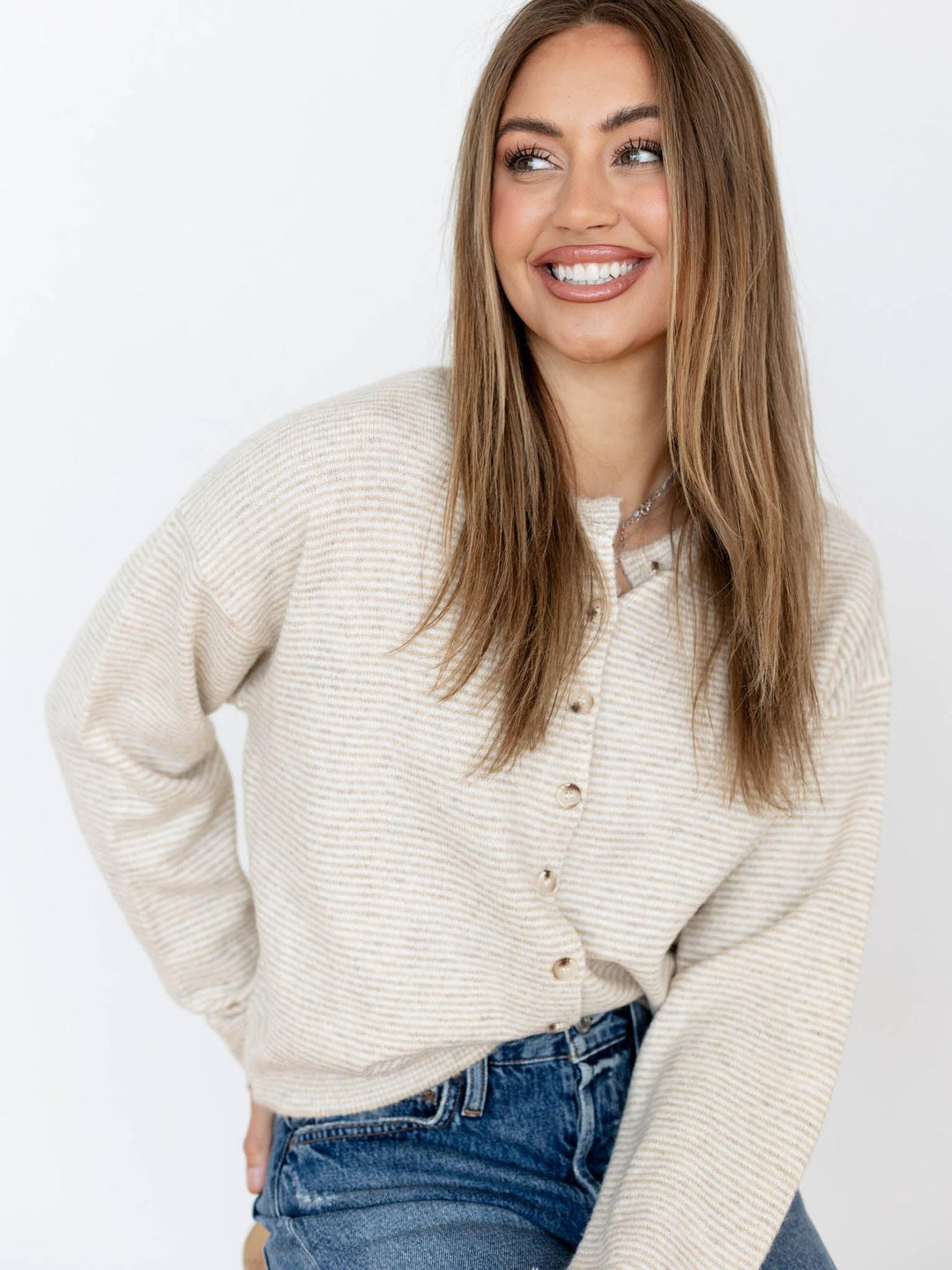 Woman wearing a cream sweater and blue jeans against a white background