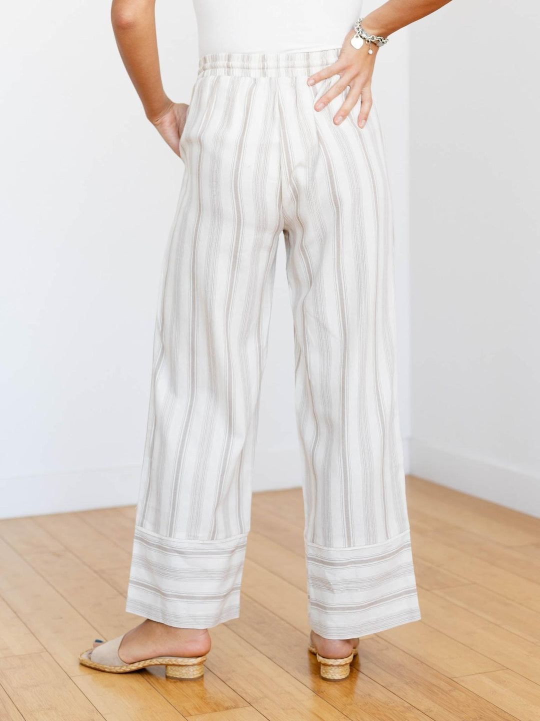 Person wearing white striped pants on a wooden floor with a white wall background