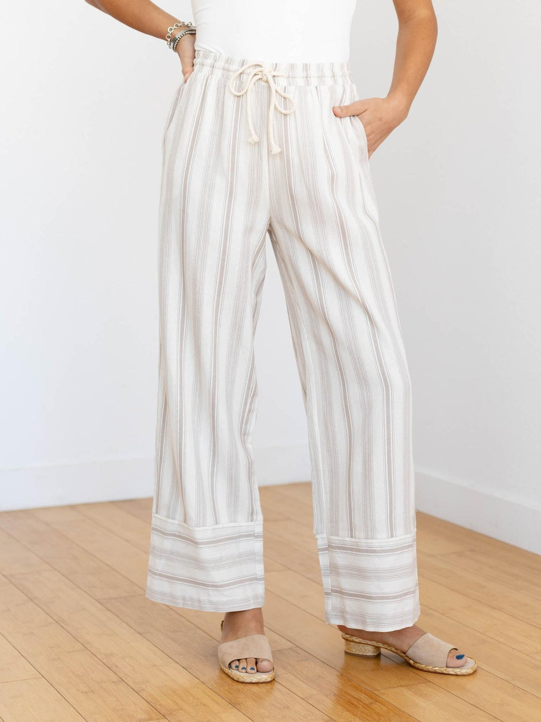 Person wearing white striped pants on a wooden floor with a white wall background