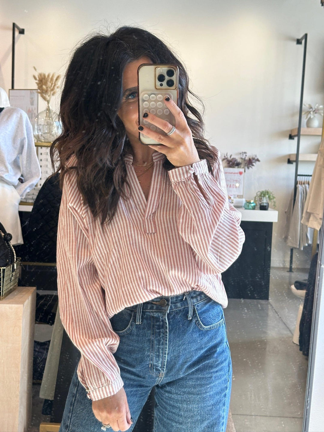 Person taking a mirror selfie wearing a striped shirt and jeans in a store.