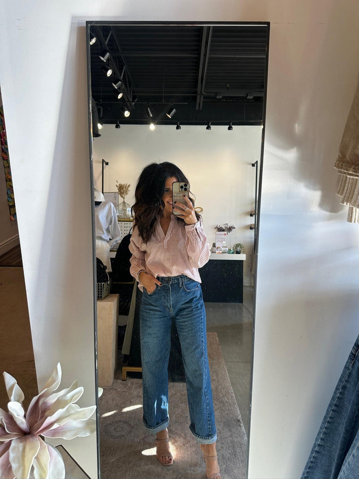 Person wearing a pink blouse and blue jeans standing in front of a mirror.