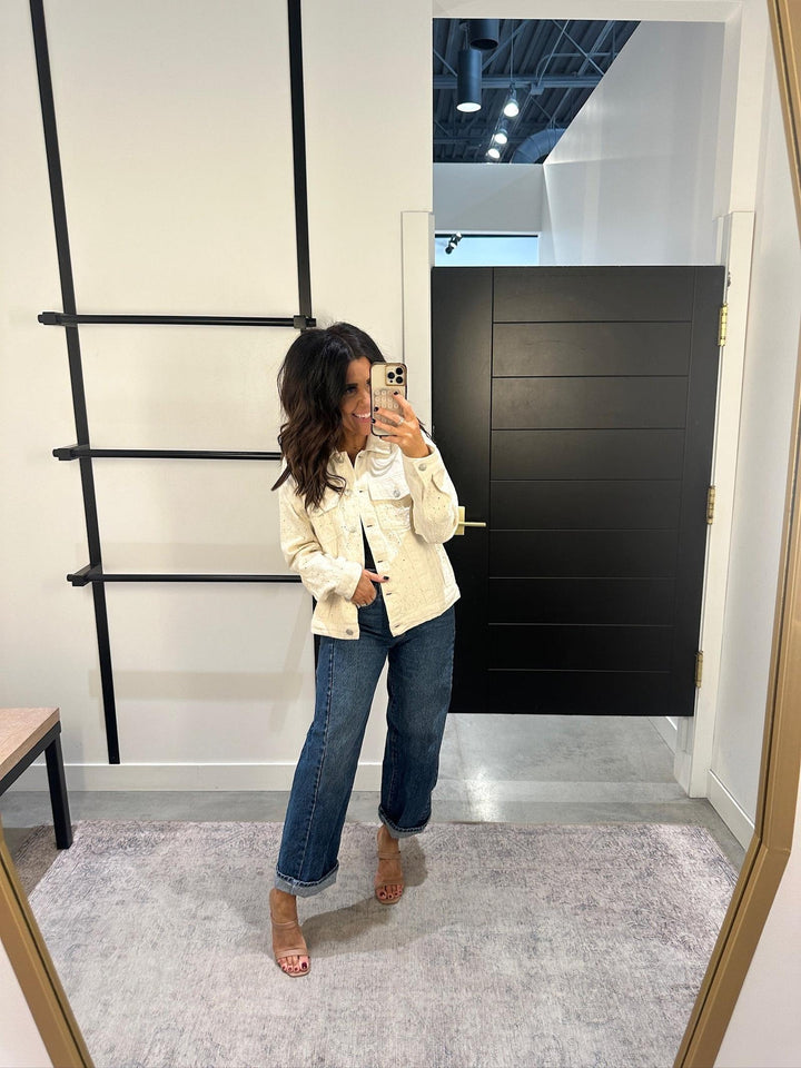 Woman taking a mirror selfie wearing a cream jacket and blue jeans in a room with a black door and ladder.