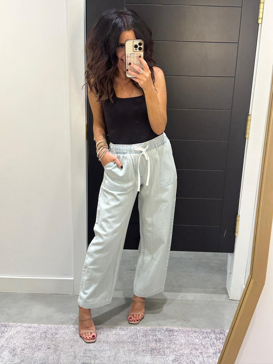 Woman taking a mirror selfie wearing a black top and light gray pants.