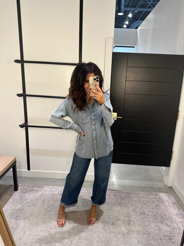 Person taking a mirror selfie wearing a denim shirt and jeans in an indoor setting.