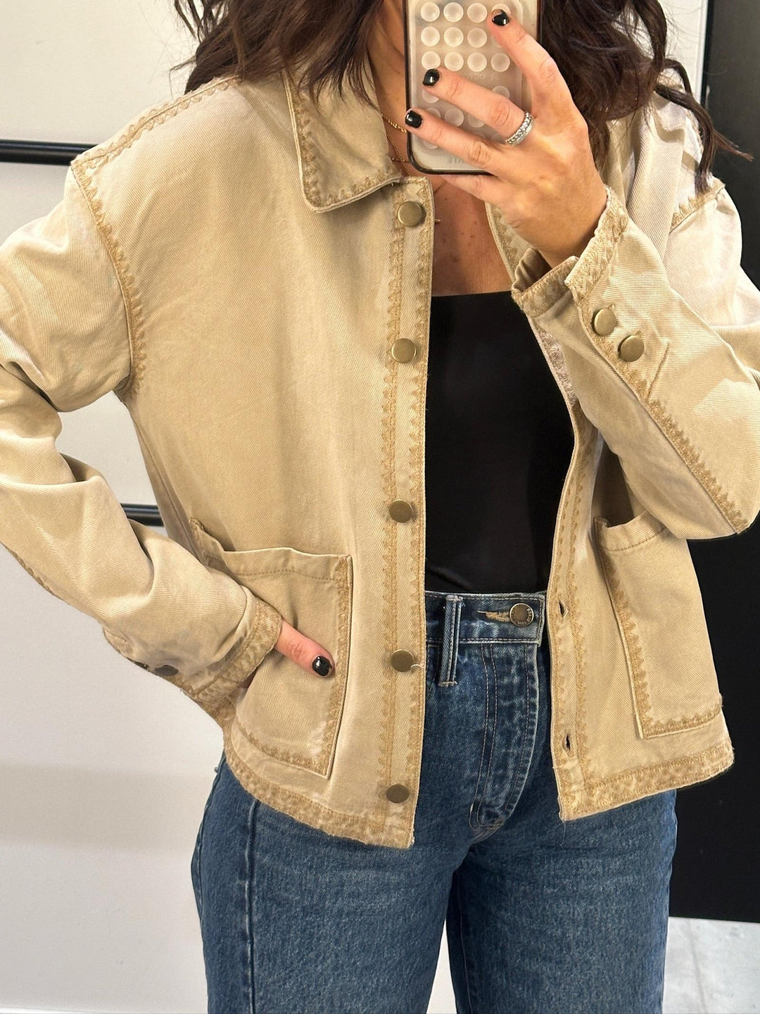 Person wearing a beige jacket and blue jeans, taking a mirror selfie.