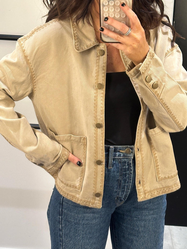 Person wearing a beige jacket and blue jeans, taking a mirror selfie.