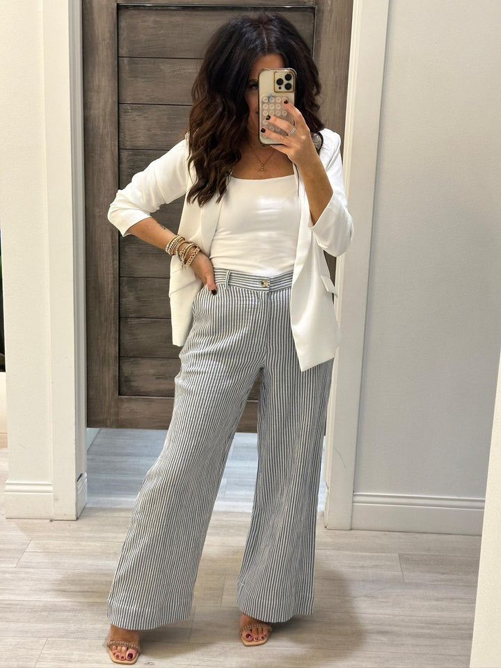 Woman taking a mirror selfie wearing a white top, light-colored cardigan, and striped pants.