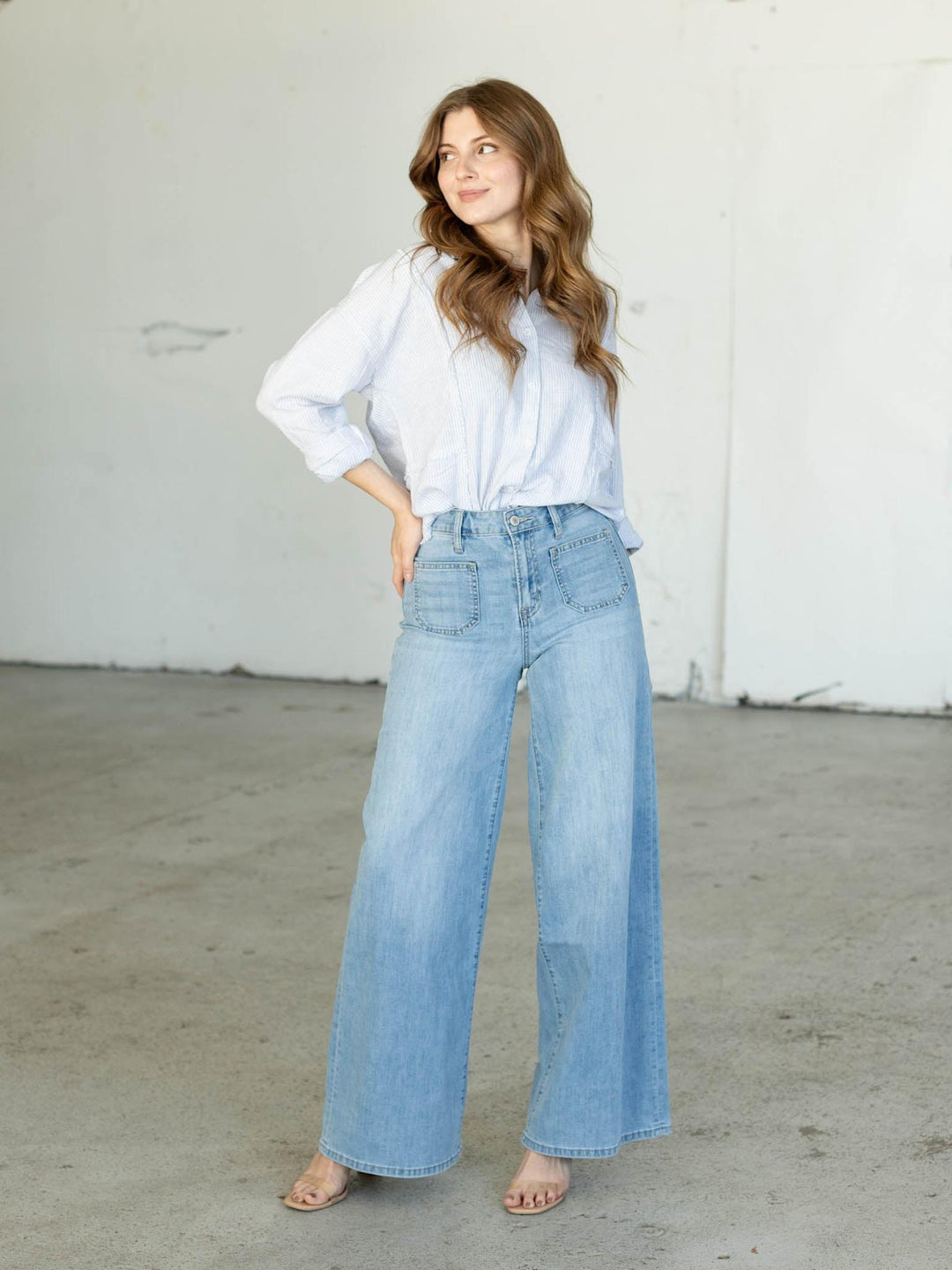 Woman wearing a light blue shirt and wide-leg jeans against a white wall.