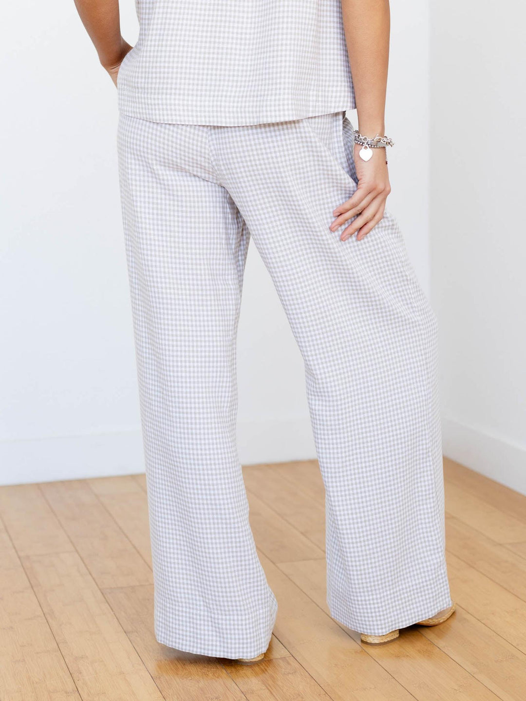 Person wearing checkered pants and a white top on a wooden floor with a white wall background