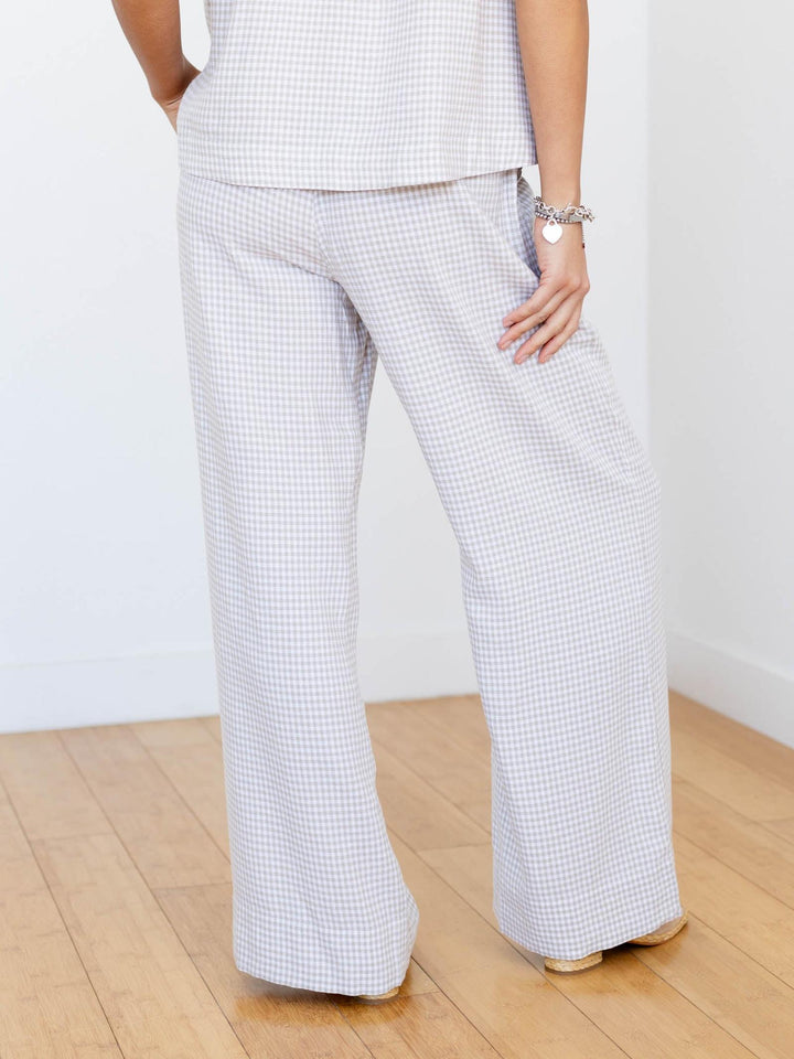 Person wearing checkered pants and a white top on a wooden floor with a white wall background