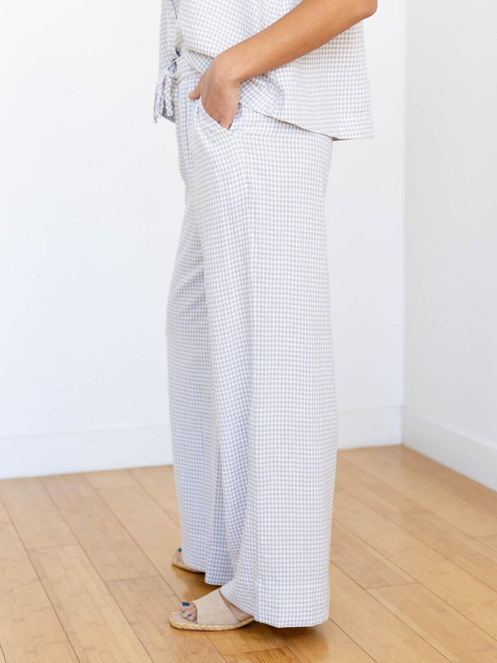 Person wearing white checkered pants on a wooden floor with a white wall background