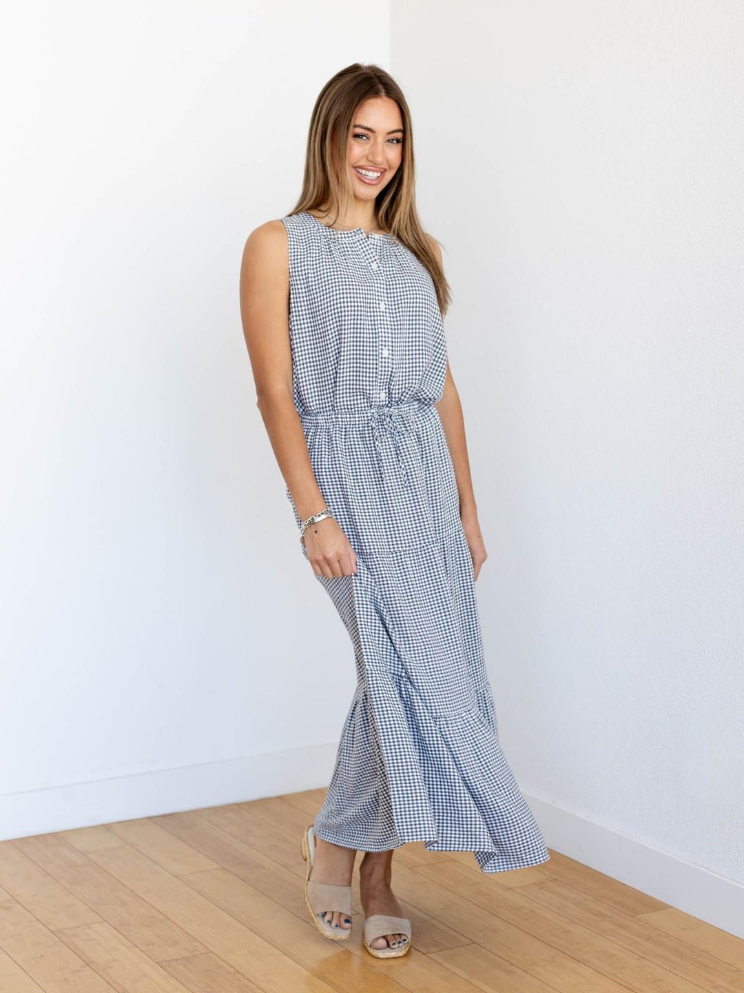 Woman wearing a blue checkered dress against a white wall.