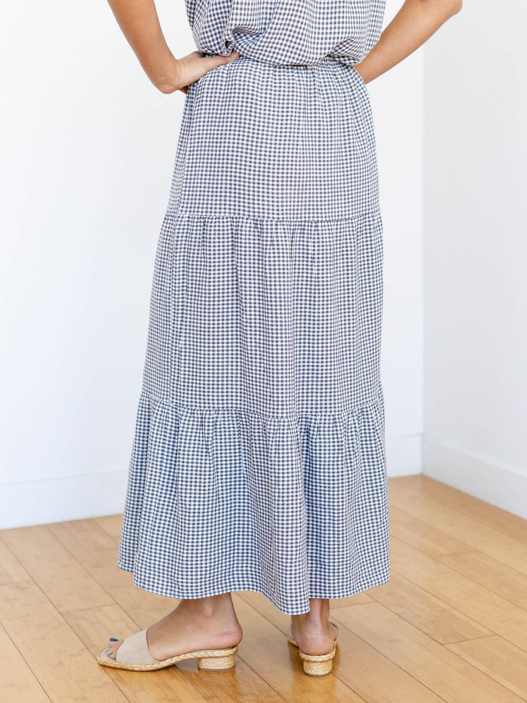 Person wearing a blue and white checkered dress on a wooden floor with a white wall background