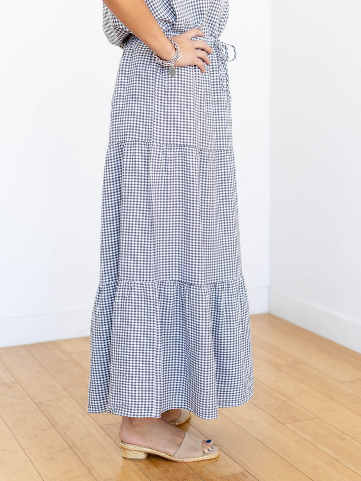 Person wearing a blue and white checkered dress on a wooden floor with a white wall background