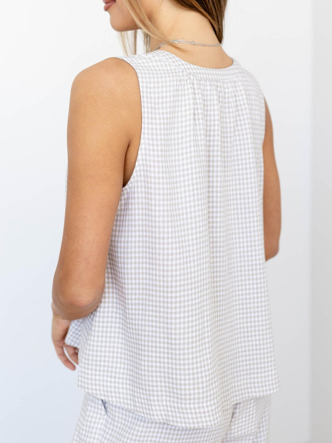 Woman wearing a white checkered sleeveless top against a light background