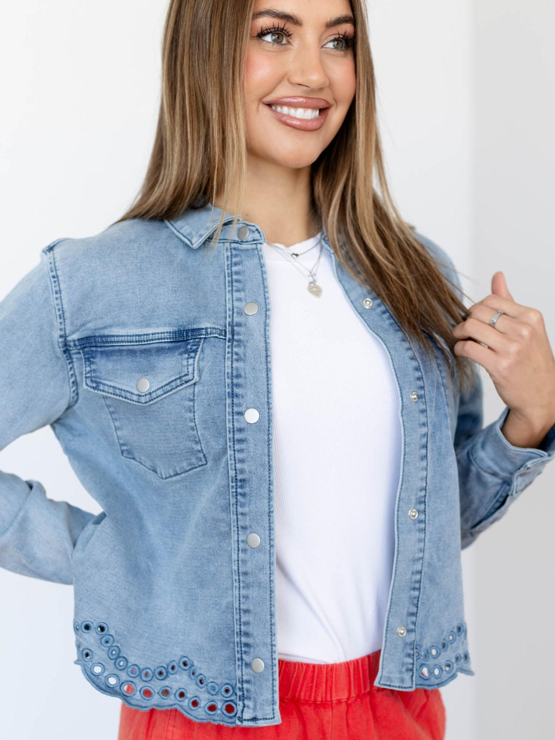 Woman wearing a light blue denim jacket over a white shirt with a red skirt on a plain background