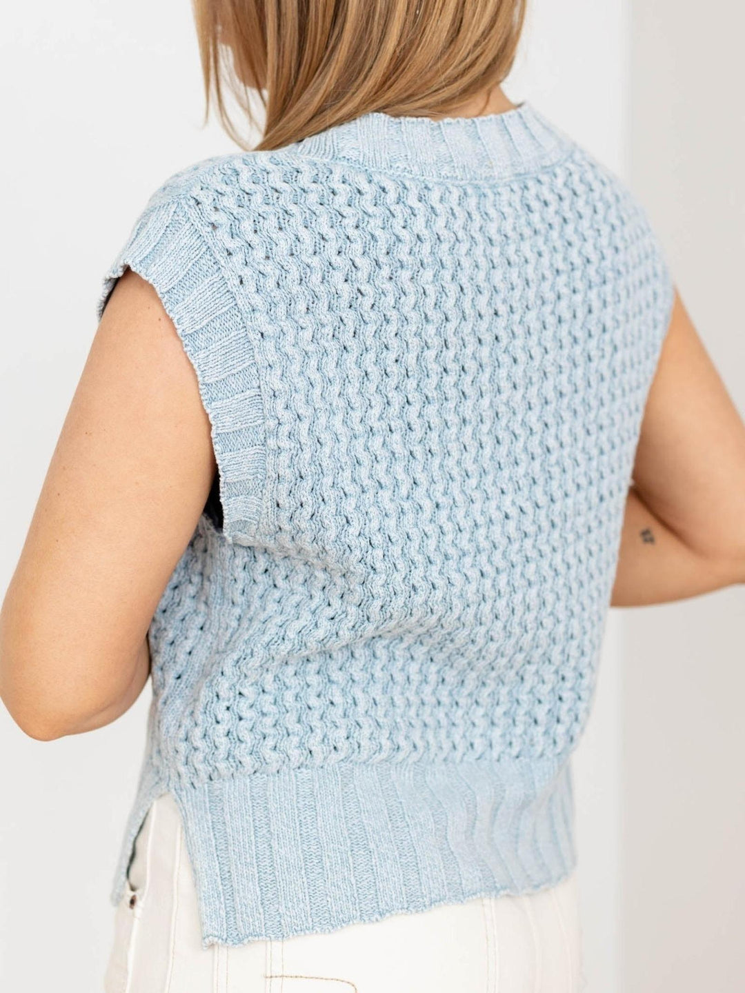 Light blue knitted vest worn by a person on a plain background