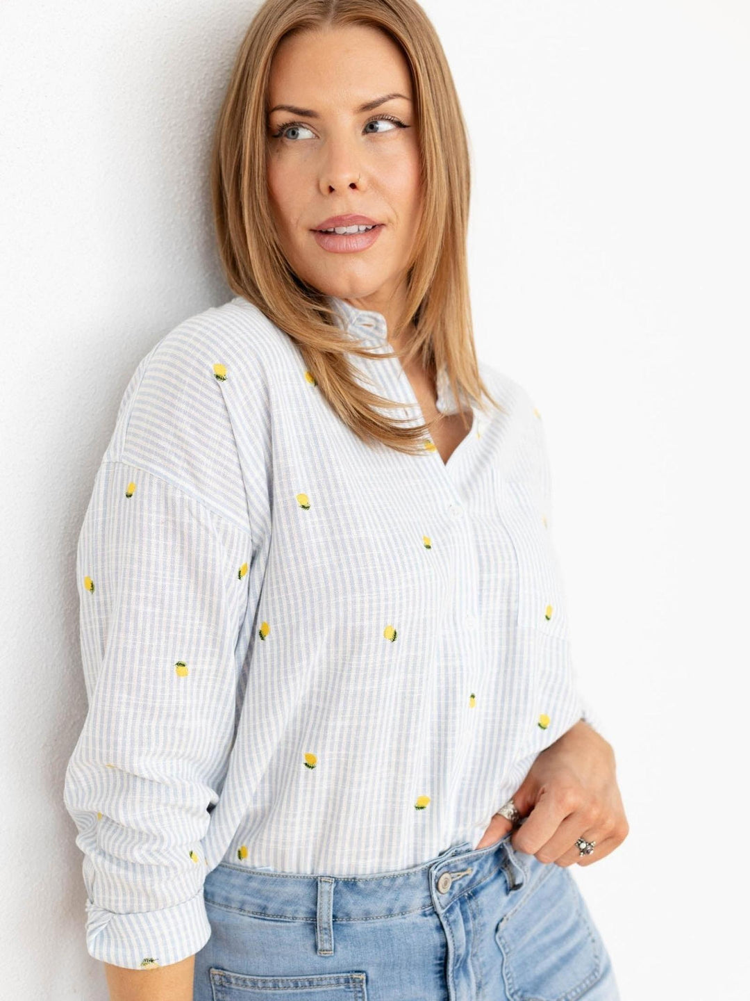 Woman wearing a white blouse with yellow polka dots and blue jeans against a light background