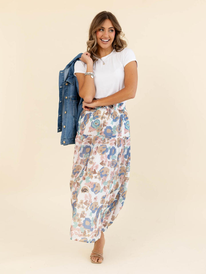 Woman wearing a white top and floral skirt with a denim jacket on a beige background