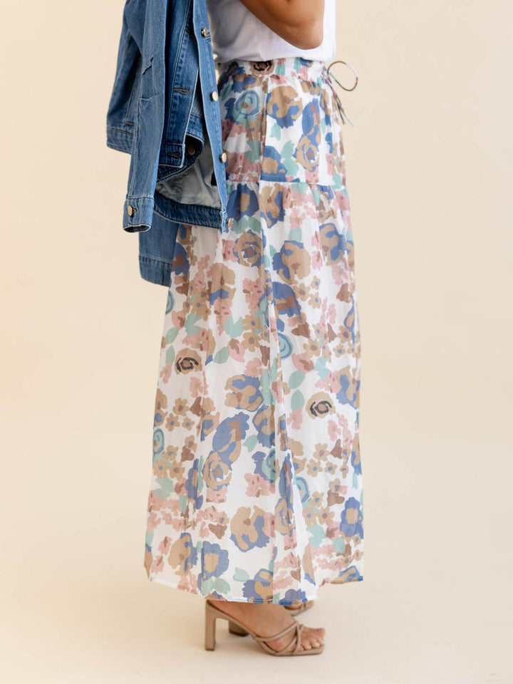 Person wearing a floral skirt with a denim jacket on a beige background