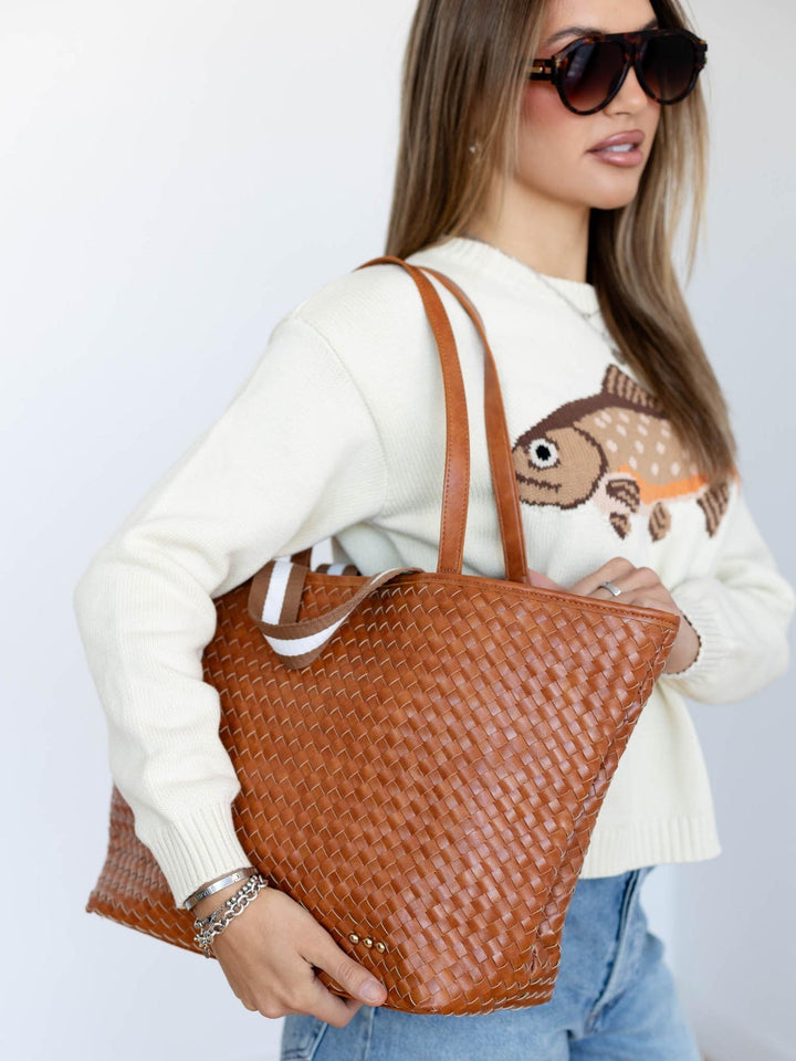 Woman holding a brown woven handbag against a plain background