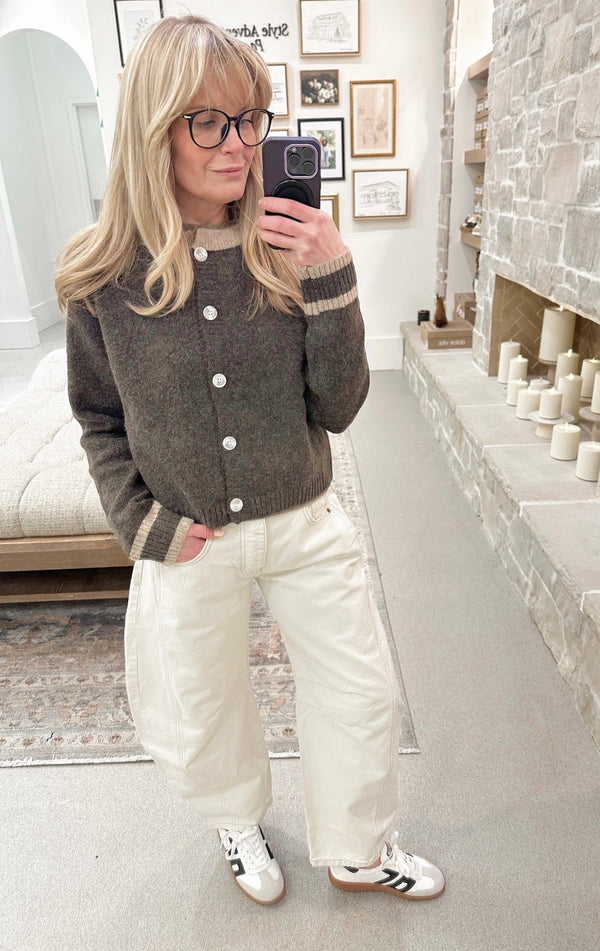 Woman taking a mirror selfie wearing a gray cardigan, white pants, and black and white sneakers in a home setting.