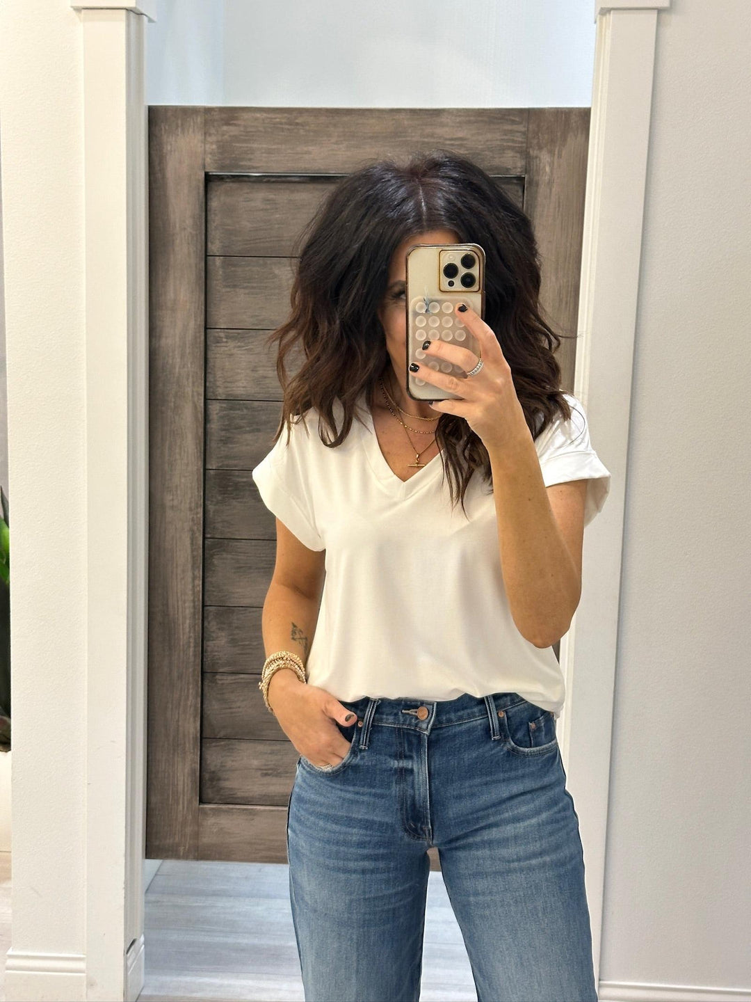 Person wearing a white top and blue jeans taking a mirror selfie.