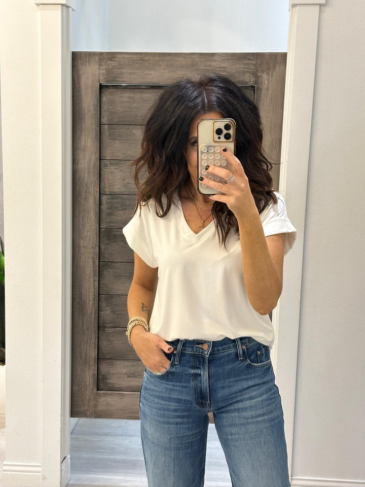Person wearing a white top and blue jeans taking a mirror selfie.