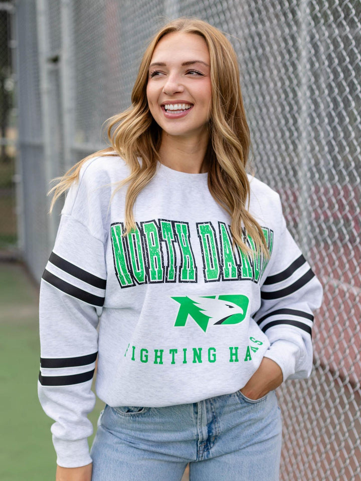 A woman smiling while wearing a white long-sleeve athletic sweatshirt with green and black lettering that reads &