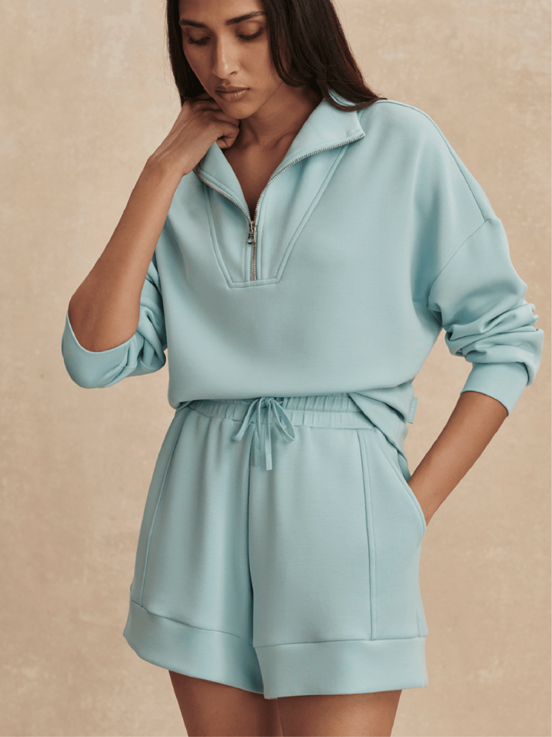 Woman wearing a light blue tracksuit against a beige background
