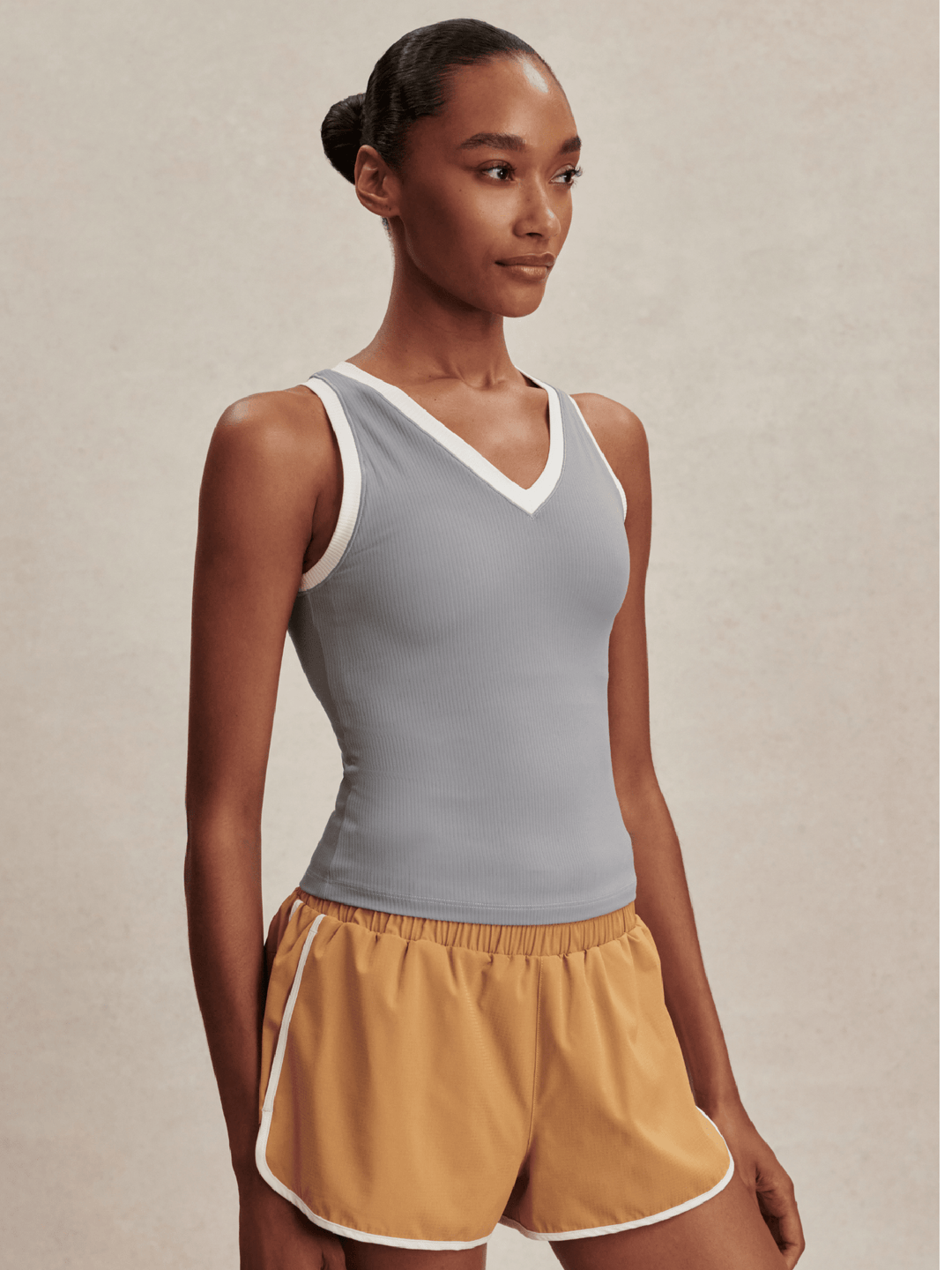 Woman wearing a gray tank top and mustard yellow shorts on a beige background