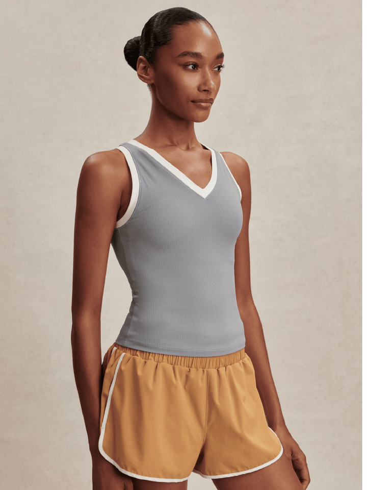 Woman wearing a gray tank top and mustard yellow shorts on a beige background
