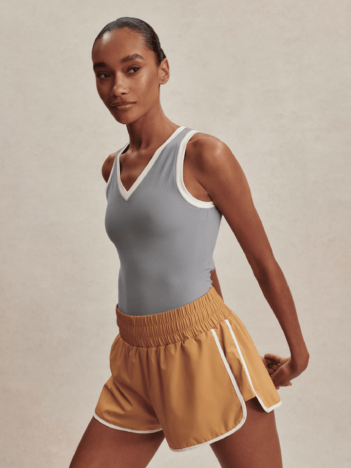 Woman wearing a gray tank top and mustard yellow shorts on a beige background