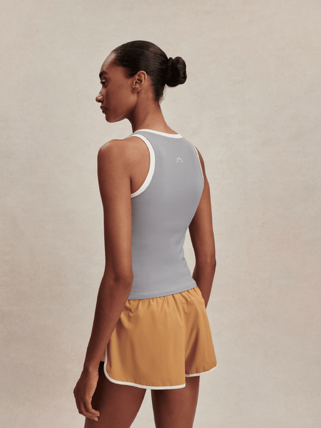 Woman wearing a gray tank top and mustard yellow shorts on a beige background