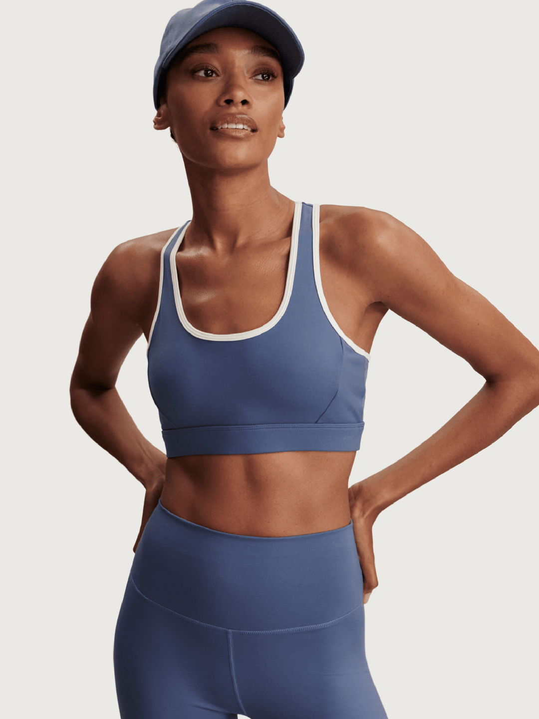 Woman wearing a blue sports bra and leggings with a matching cap on a light gray background