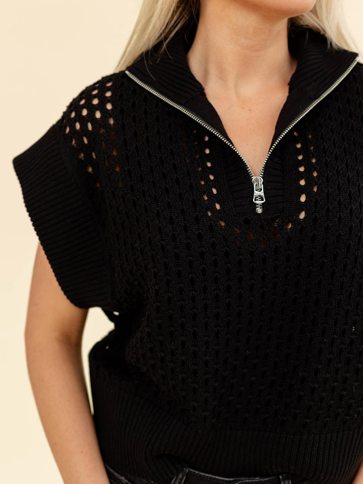 Black sleeveless sweater with openwork shoulders on a beige background