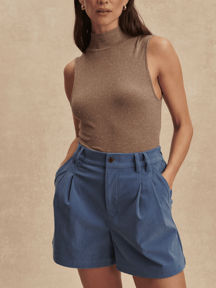 Woman wearing a brown sleeveless top and blue shorts against a beige background