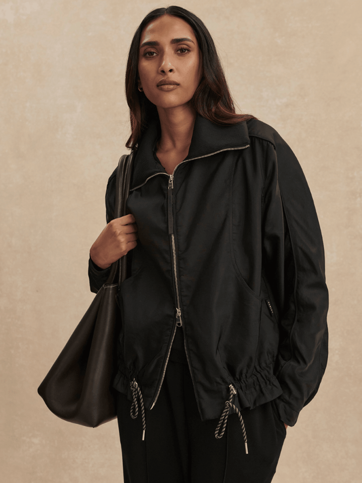 Woman wearing a black jacket and holding a matching bag against a beige background