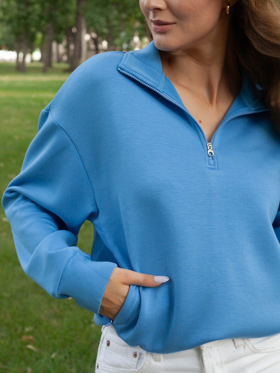 A woman wearing a bright blue long-sleeve quarter-zip sweatshirt in an outdoor park setting.