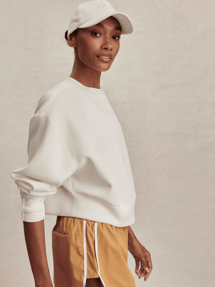 Person wearing a white sweatshirt and beige shorts with a plain background