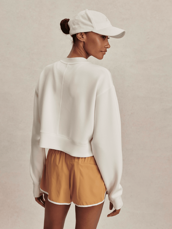 Person wearing a white sweatshirt and mustard shorts on a beige background
