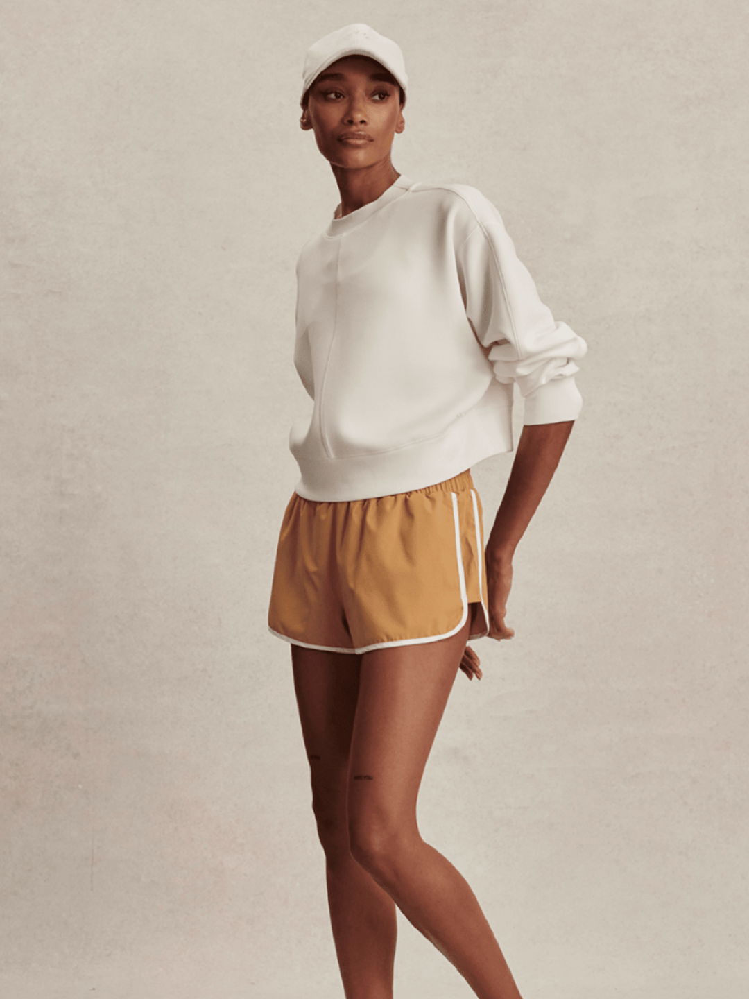 Person wearing a white sweatshirt and mustard yellow shorts on a plain background