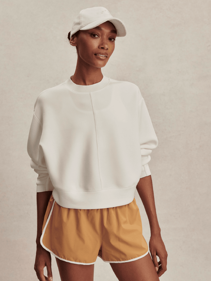 Person wearing a white sweatshirt and mustard yellow shorts on a beige background