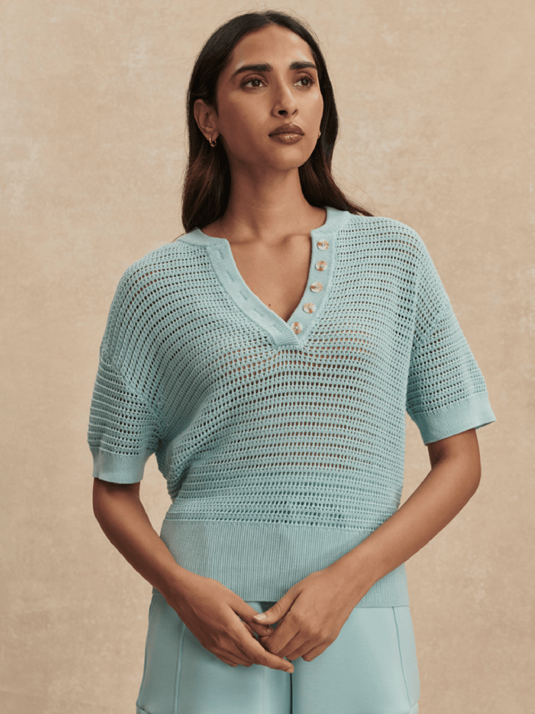 Woman wearing a light blue knit top against a beige background