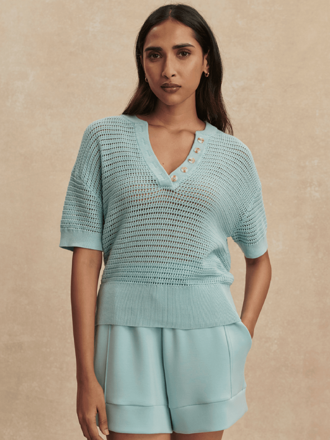 Woman wearing a light blue knit top and shorts against a beige background