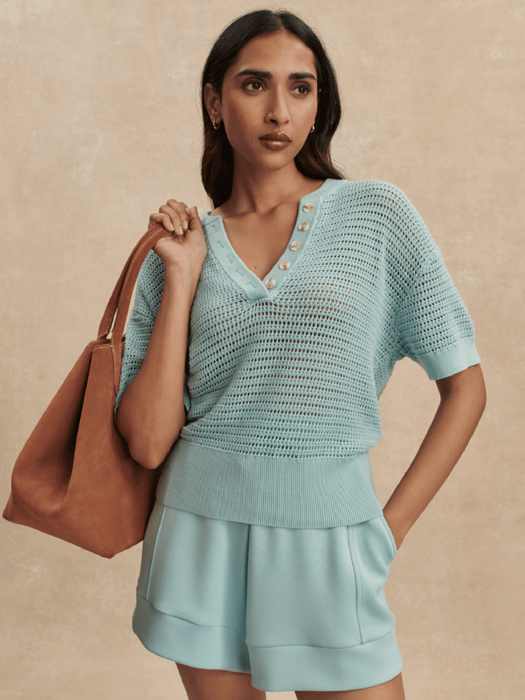 Woman wearing a light blue outfit with a brown handbag against a beige background