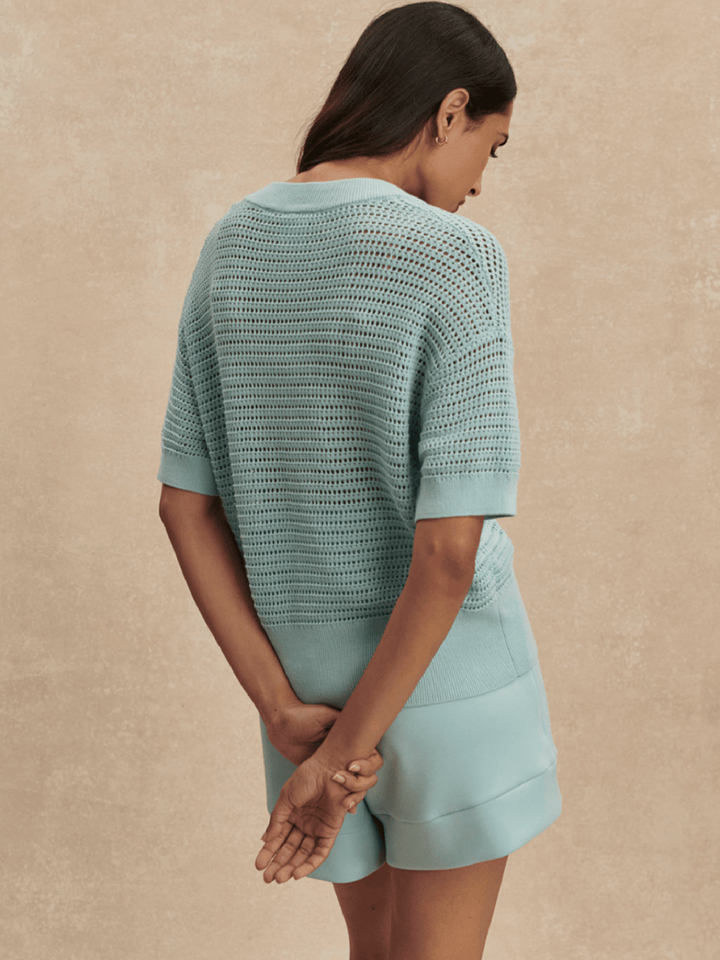 Woman wearing a light blue crochet top and shorts set against a beige background