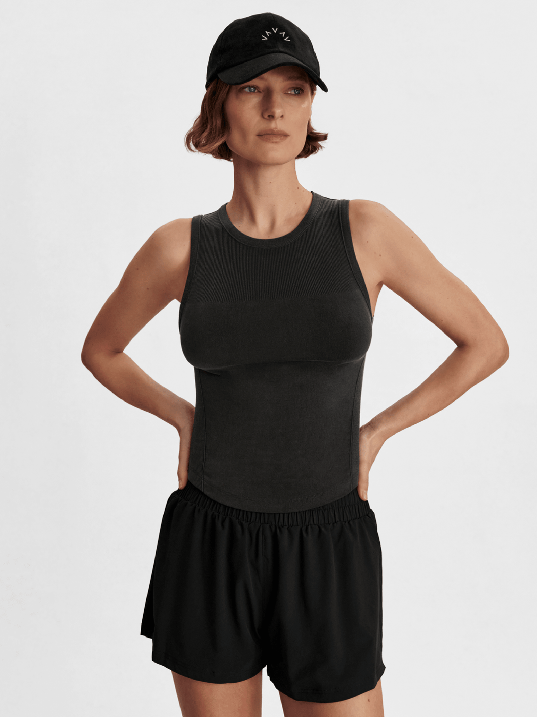 Woman wearing a black tank top and shorts with a black cap on a white background