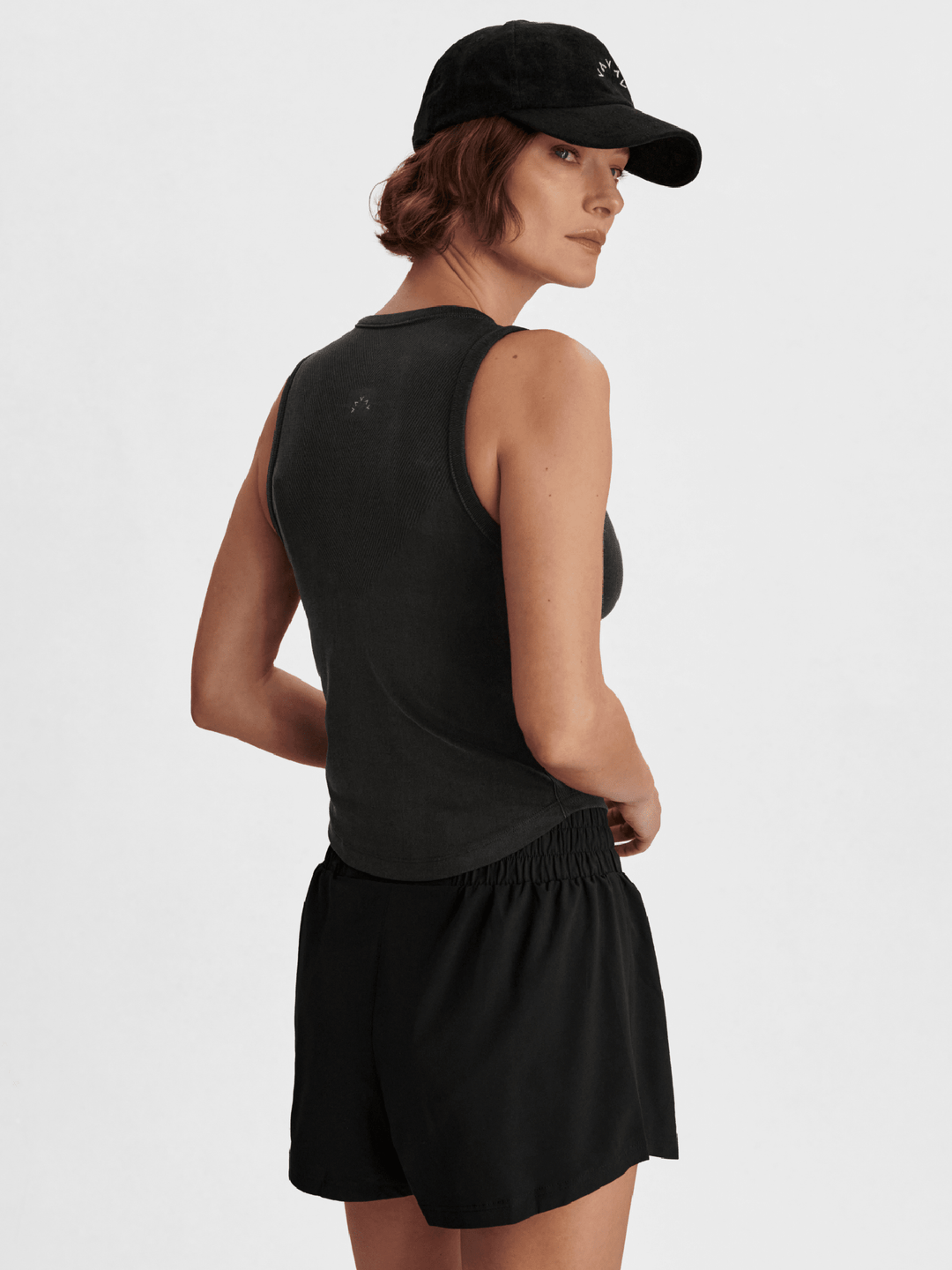 Person wearing a black sleeveless top and shorts with a cap on a neutral background