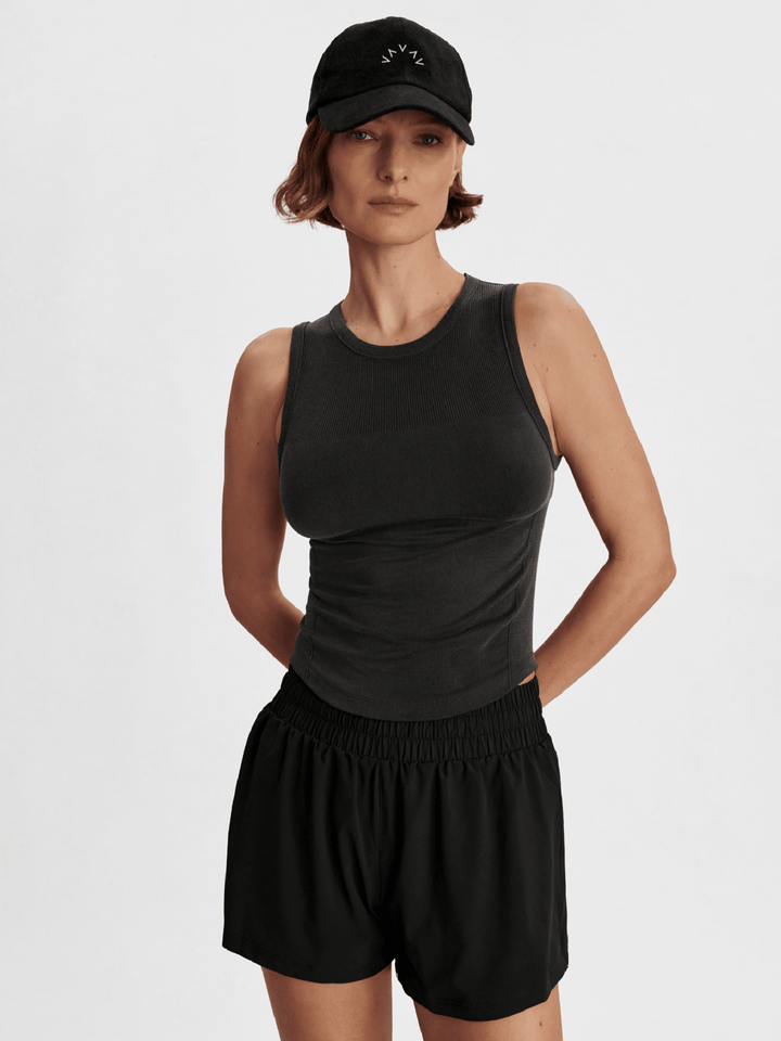 Woman wearing a black sleeveless top and shorts with a black cap on a white background